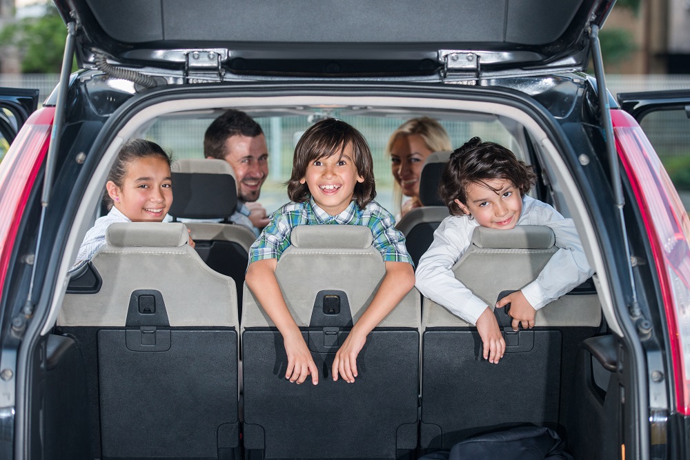 Happy smiling family in the car looking backwards through open trunk
