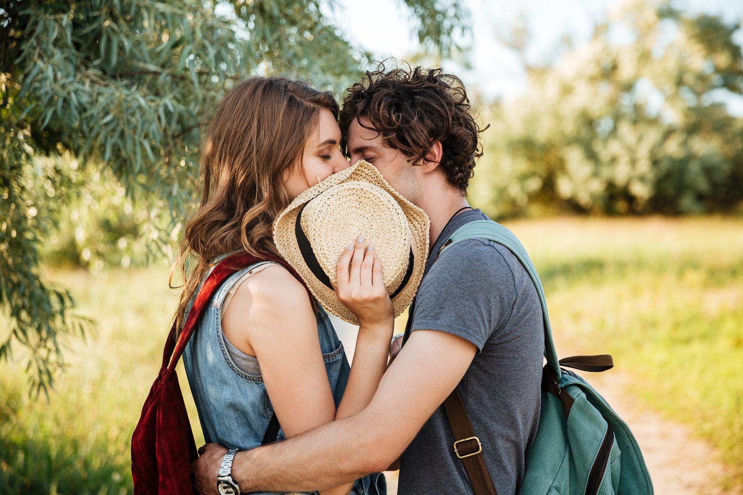 Close up portrait of a young attractive couple in love embracing with their eyes closed and kissing over forest background