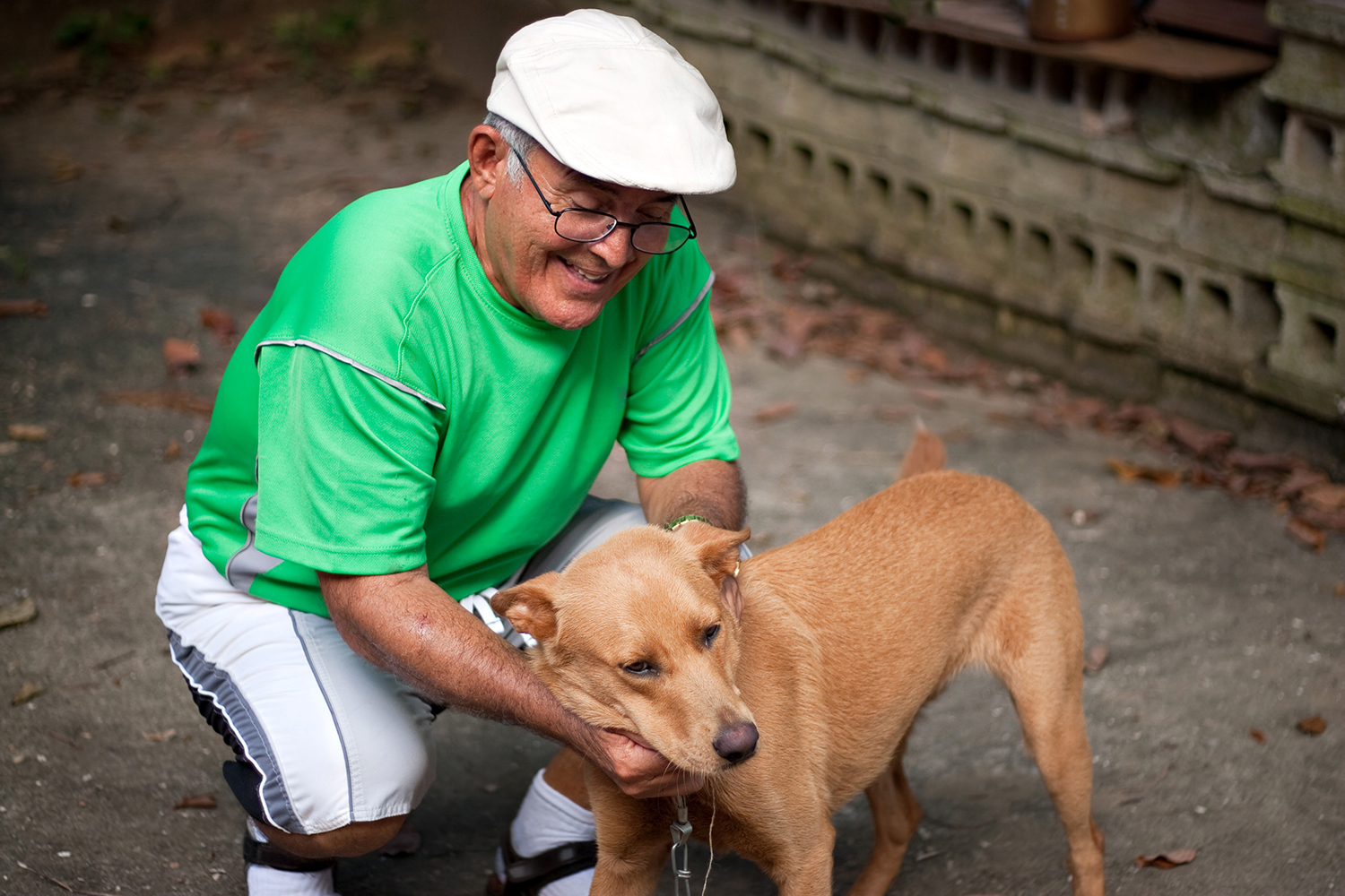 An elderly Hispanic senior citizen man petting his dog with a large smile on his face.